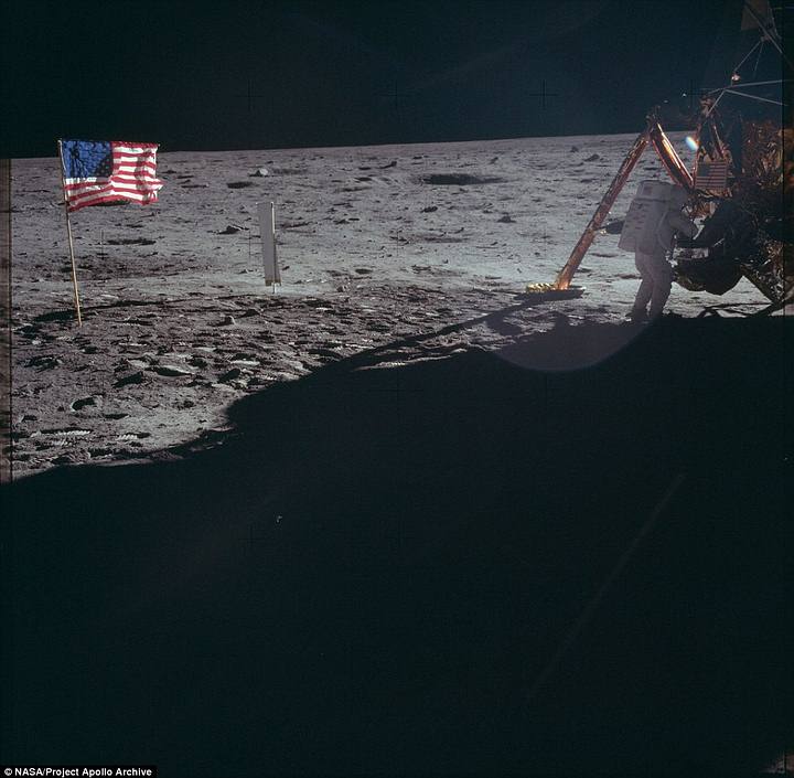 Uno de los astronautas manipula el módulo lunar mientras la bandera estadounidense se muestra tras de él.