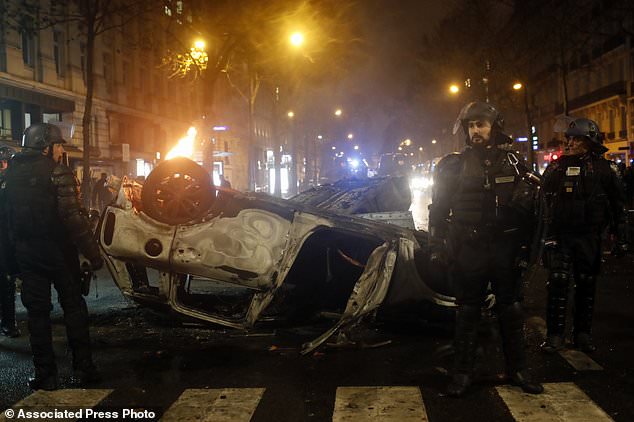 Riot police officers stand next to charred cars near the Trocadero square after a demonstration Saturday, Dec.1, 2018 in Paris. A protest against rising taxes and the high cost of living turned into a riot Saturday in Paris as police fired tear gas and water cannon in street battles with activists wearing the fluorescent yellow vests of a new movement. (AP Photo/Thibault Camus)